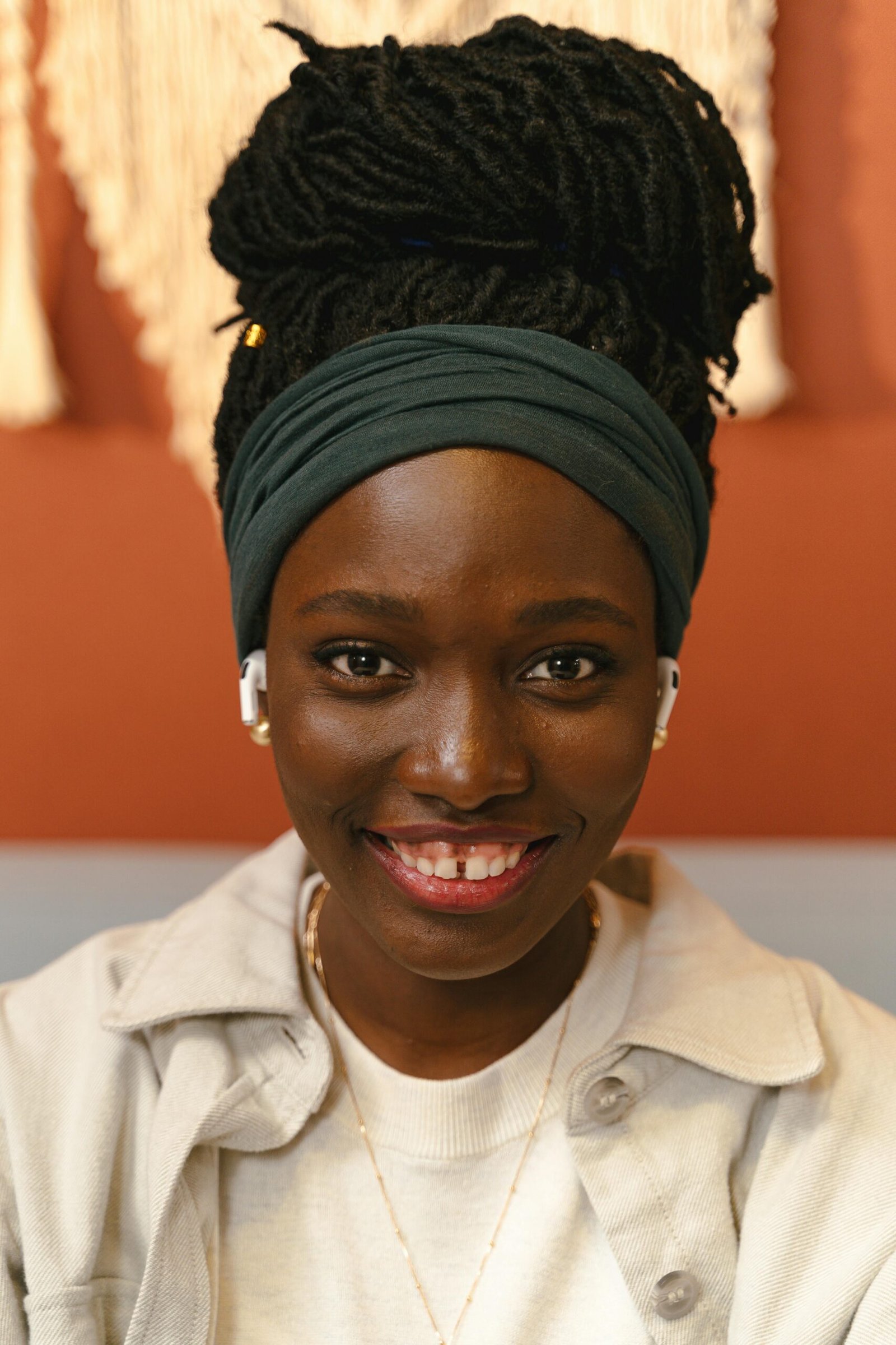 Portrait of a young woman with braided hair, smiling while wearing wireless earphones indoors.